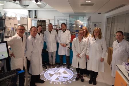 Members of the Technician Steering Committee wearing labcoats gather around an image of the University of Edinburgh's crest at the Genome Foundry